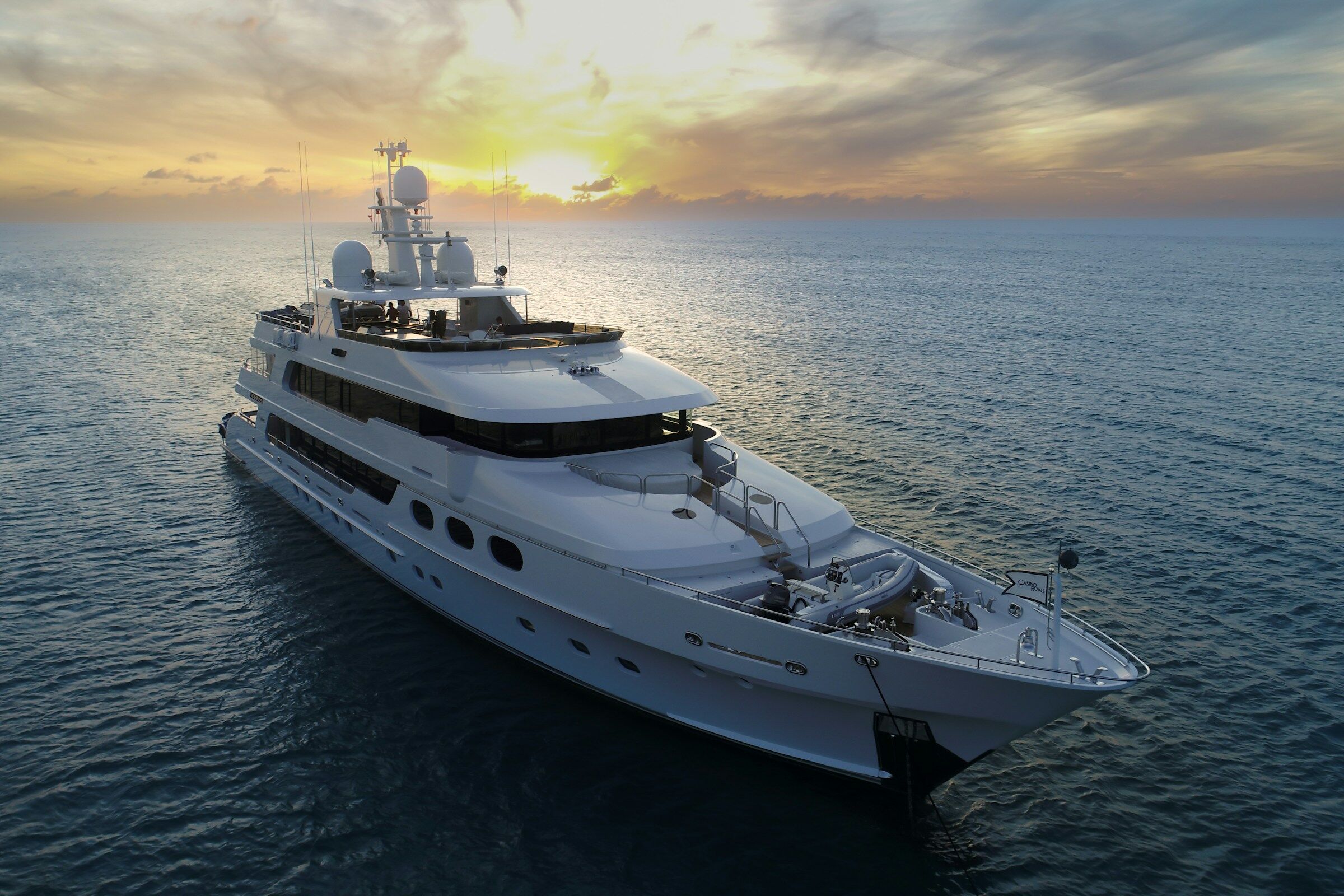 A crewed motor yacht under way on open water with the sun low behind her