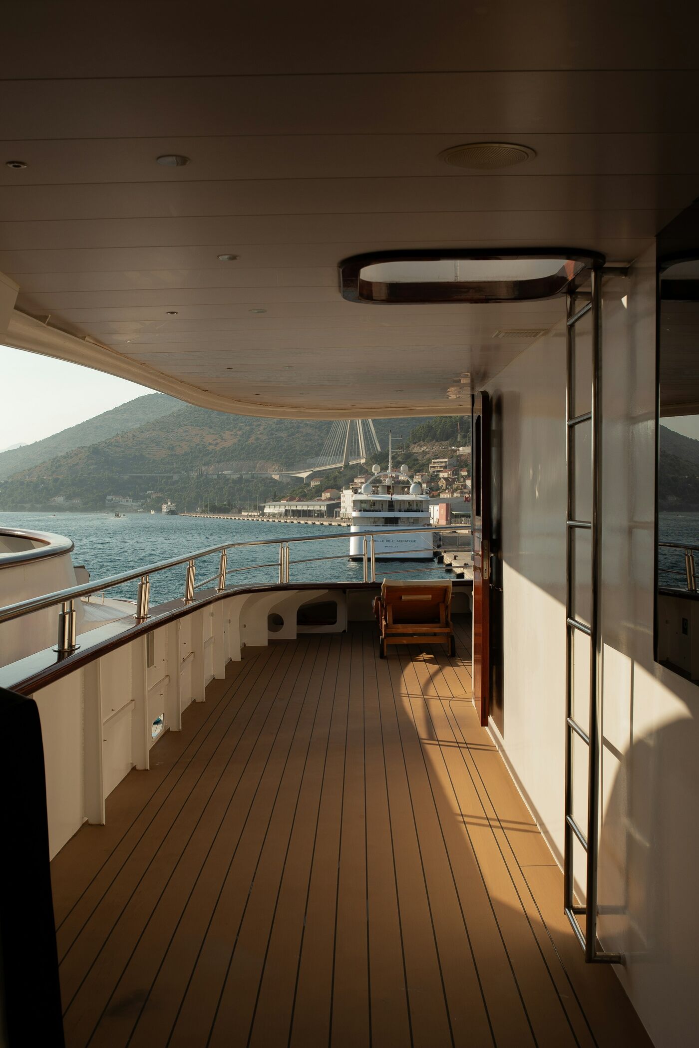 The covered side deck of a yacht, teak underfoot and the sea beyond the rail