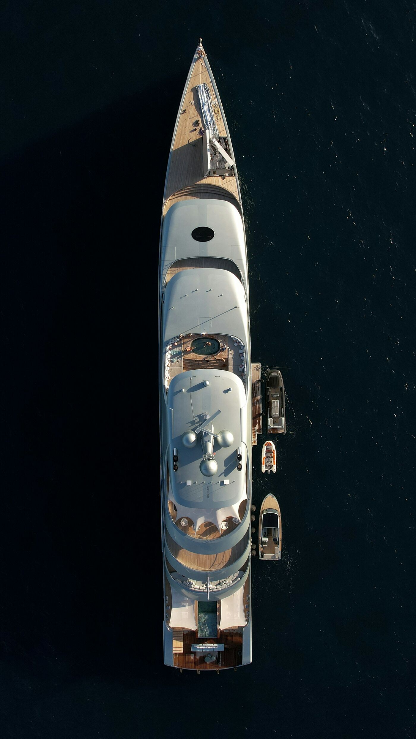 A superyacht under way on dark water, photographed straight down from a drone