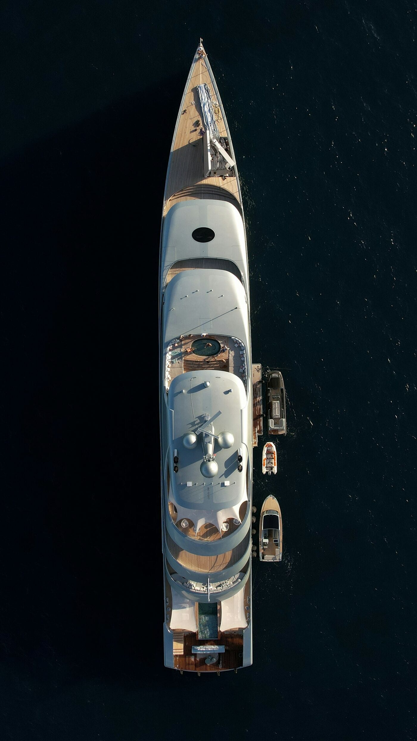 A superyacht under way on dark water, photographed straight down from a drone